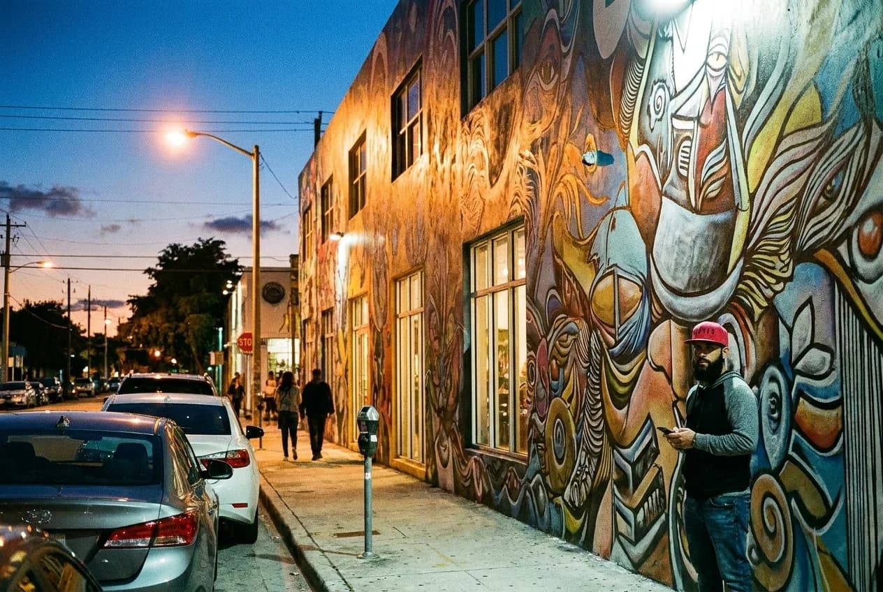 Wynwood mural wall at dusk with streetlights and parked cars along metered curb