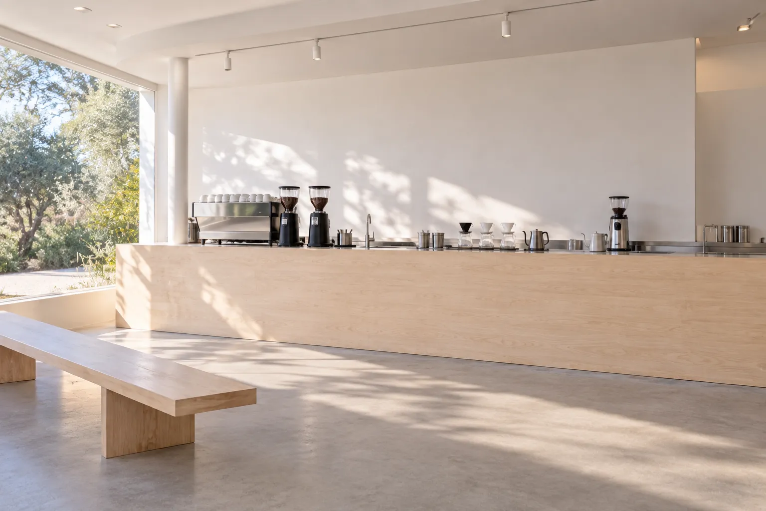 Extremely pared-back café interior with white walls, a pale timber counter, one long bench and brewing equipment as the only visual focus