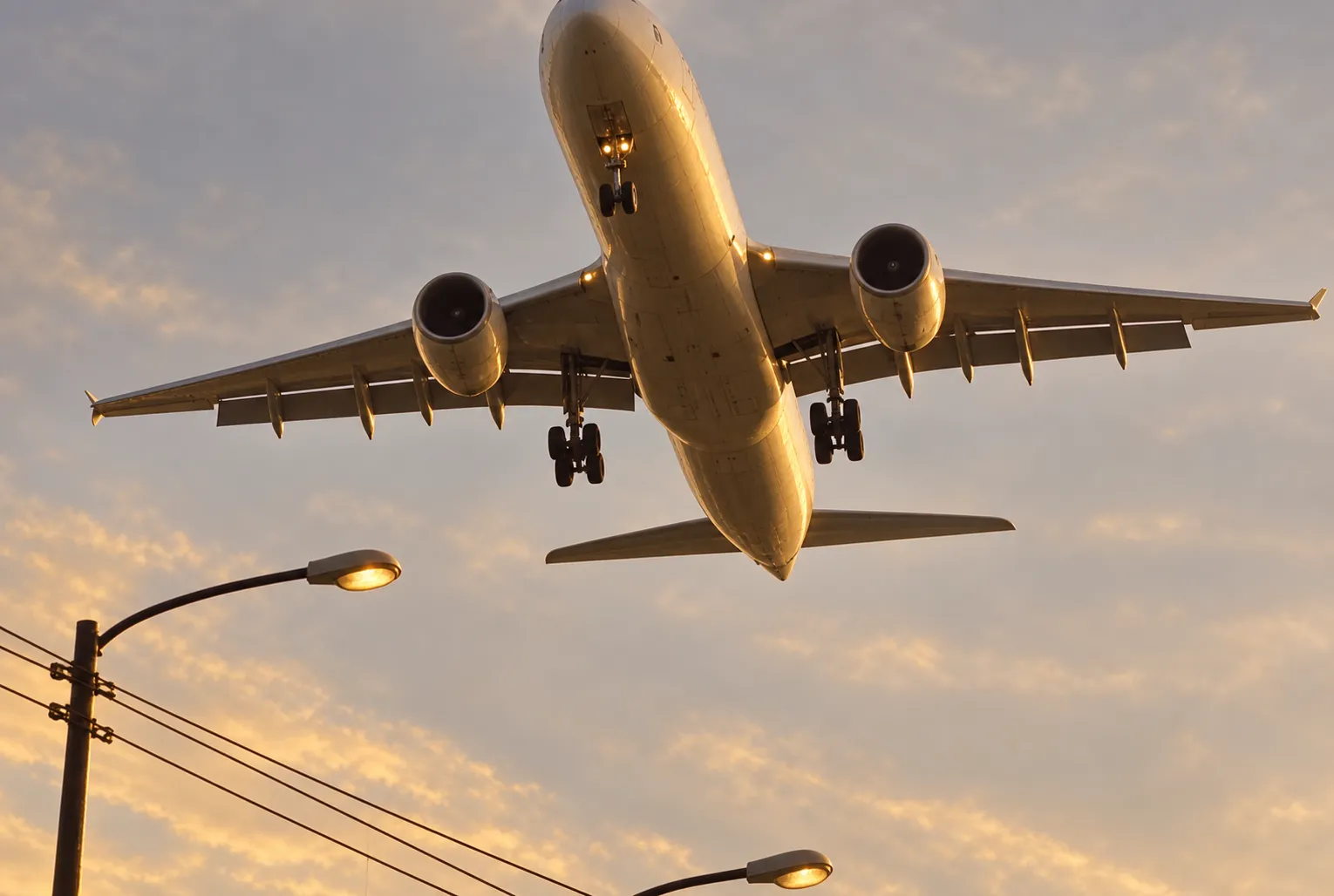 A wide-body aircraft low overhead against a pale evening sky