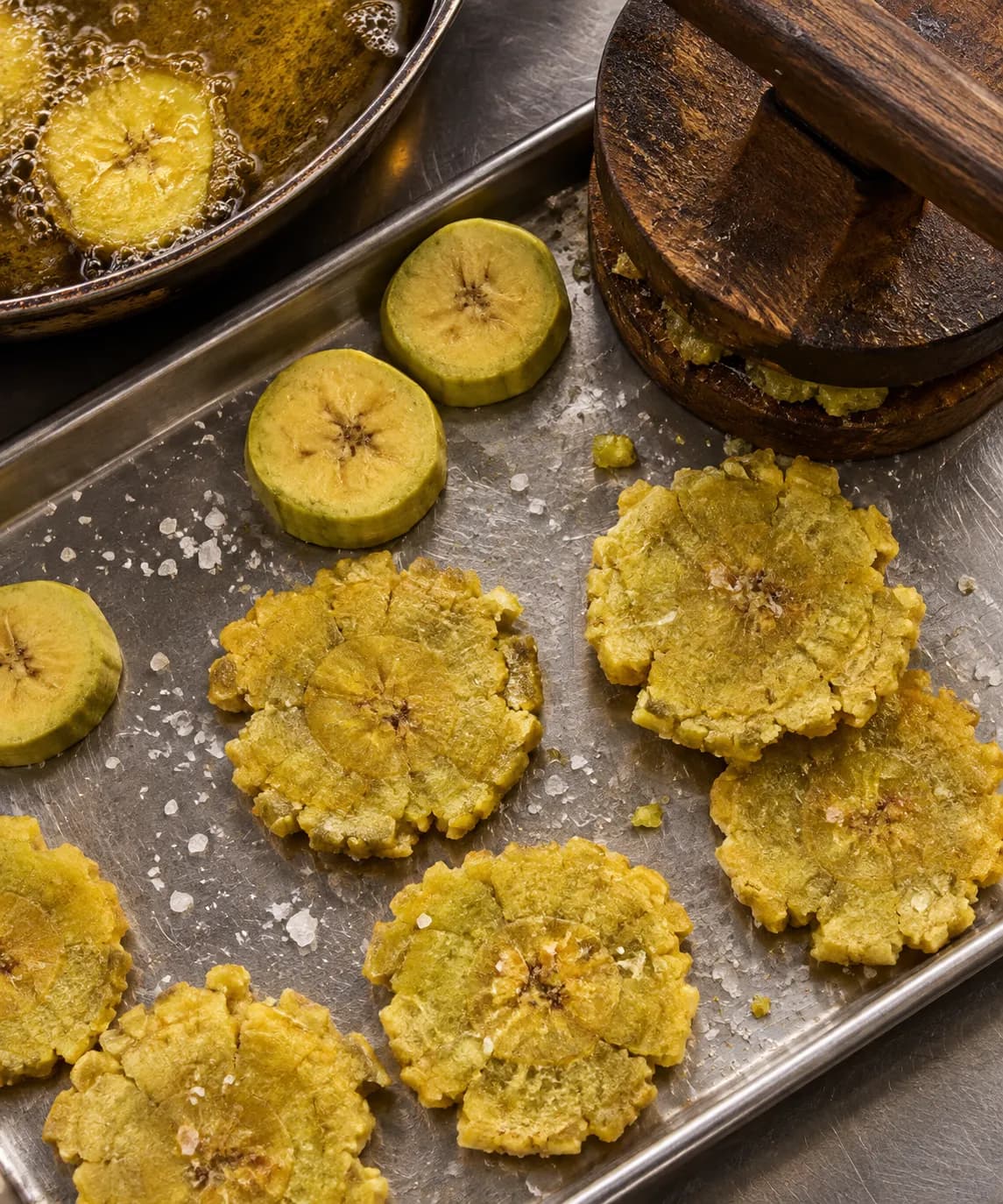 Green plantains being pressed flat before frying