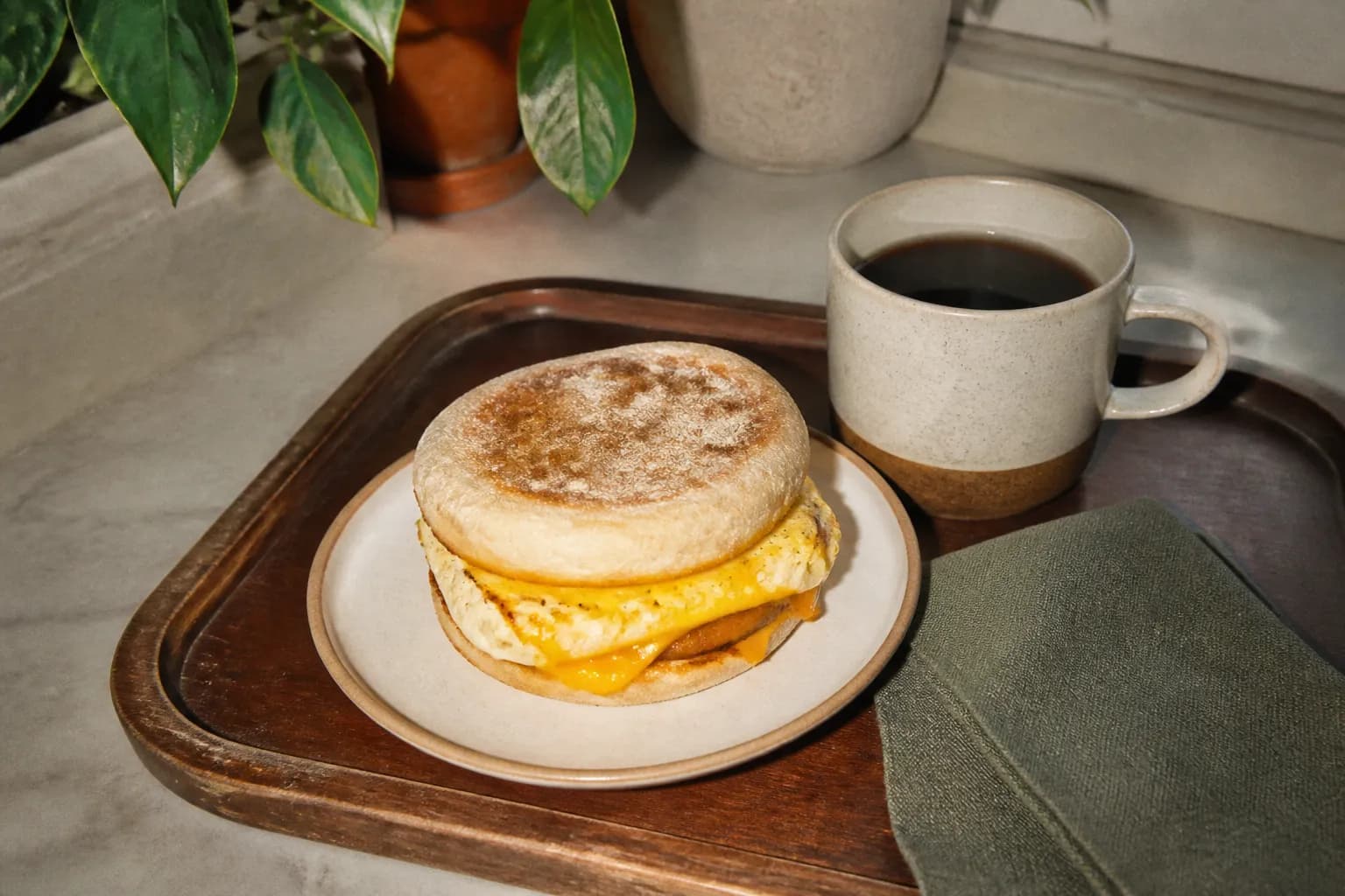 An egg breakfast sandwich beside a cup of coffee on a tray