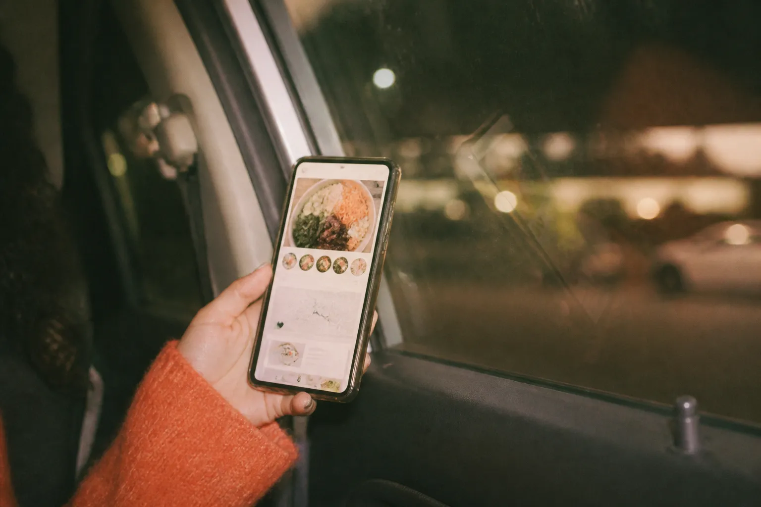 A phone showing an order screen held beside a car window at a drive-thru