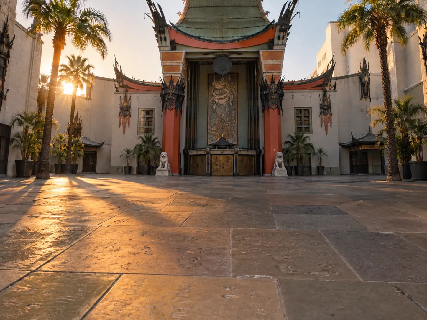 Ornate pagoda-style theatre facade seen across its paved forecourt with red columns, a curved roofline and handprint slabs set into the paving
