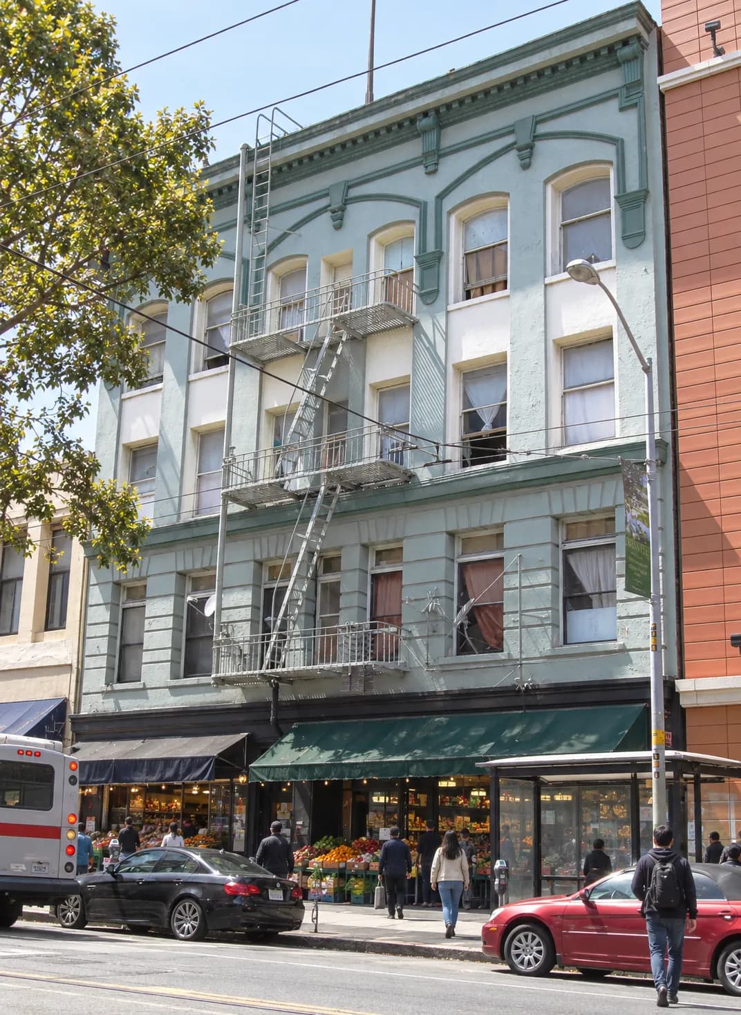 Busy working commercial street with two- and three-storey mixed-use buildings, painted frontages, awnings and overhead trolley wires