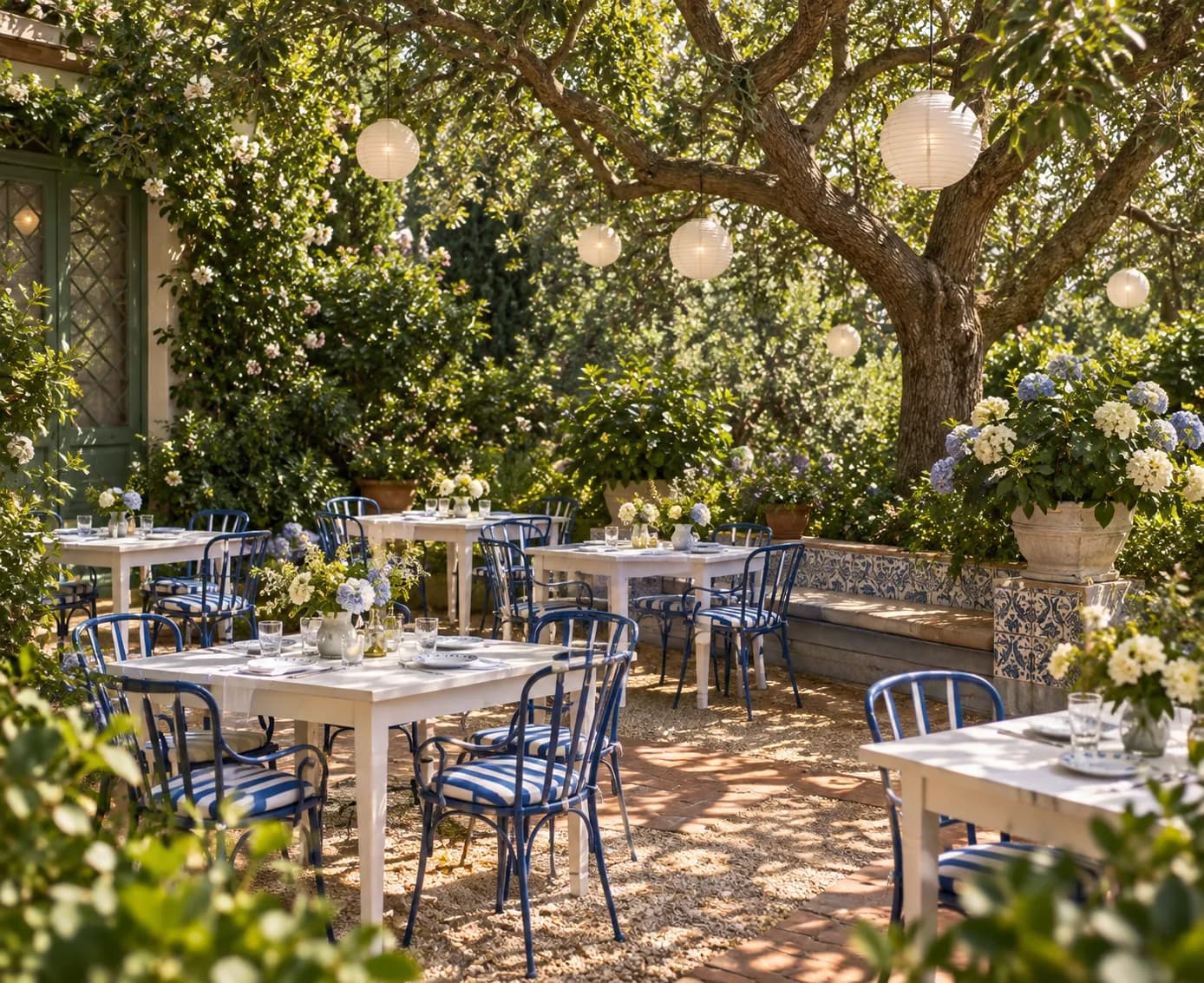 A garden terrace with white tables and chairs beneath a large tree