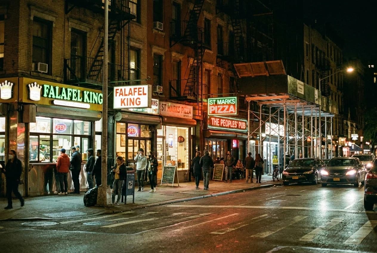 Night view of St Marks Place in the East Village with neon signs above falafel counters and small restaurants