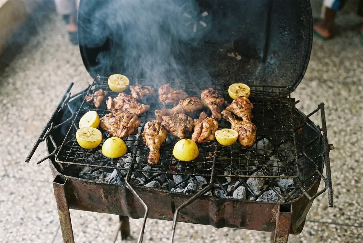 Grilled meat and lemon halves on a charcoal grill with smoke rising