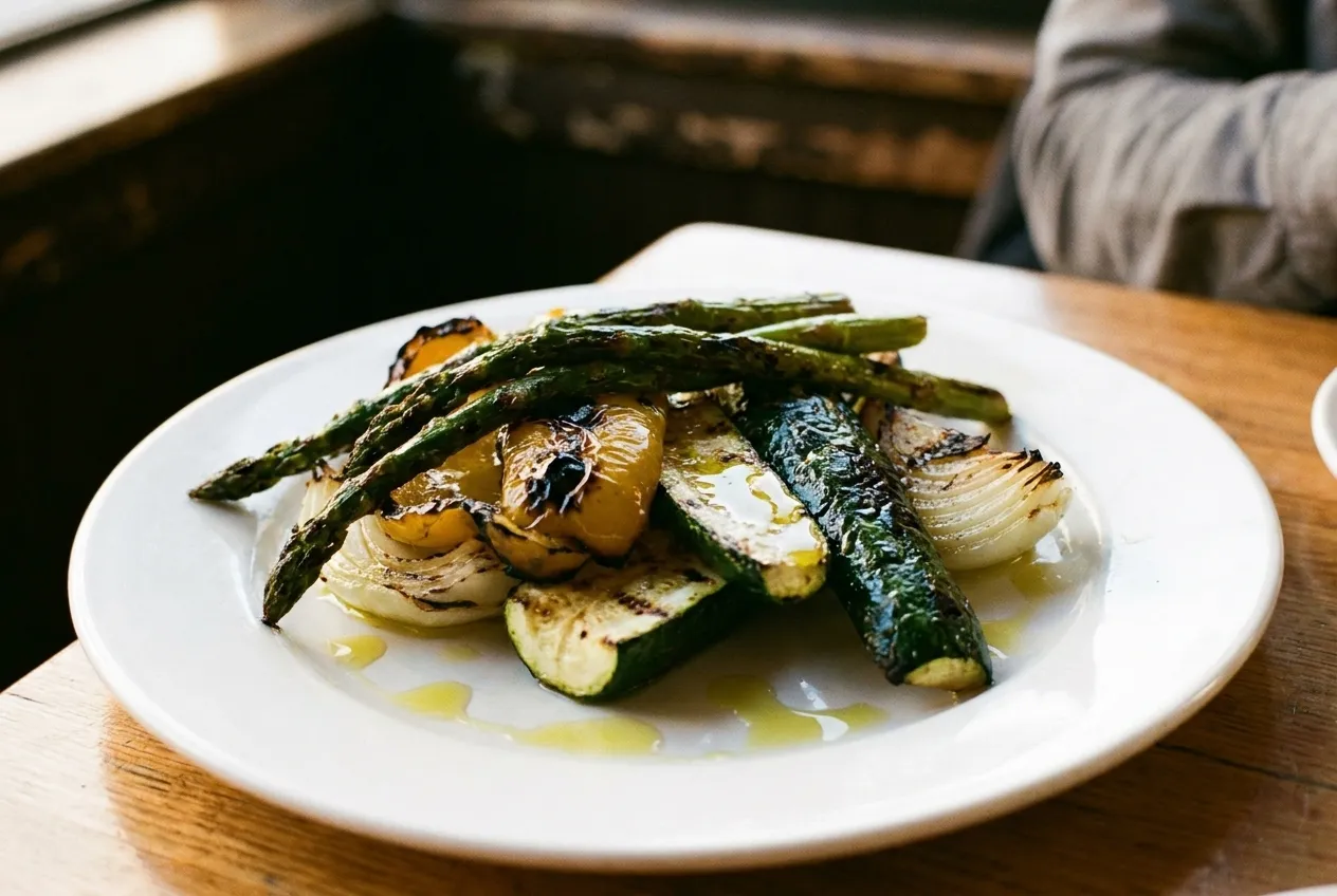 Charred grilled vegetables piled on a white plate, blackened edges and a drizzle of oil catching the light