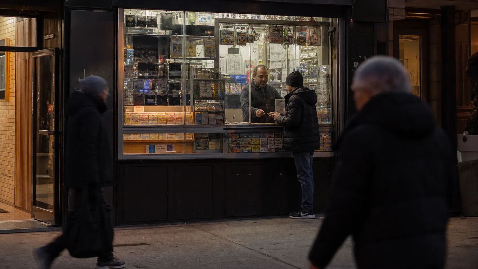 A New York City convenience store at dusk with people passing outside and a lottery counter visible inside.