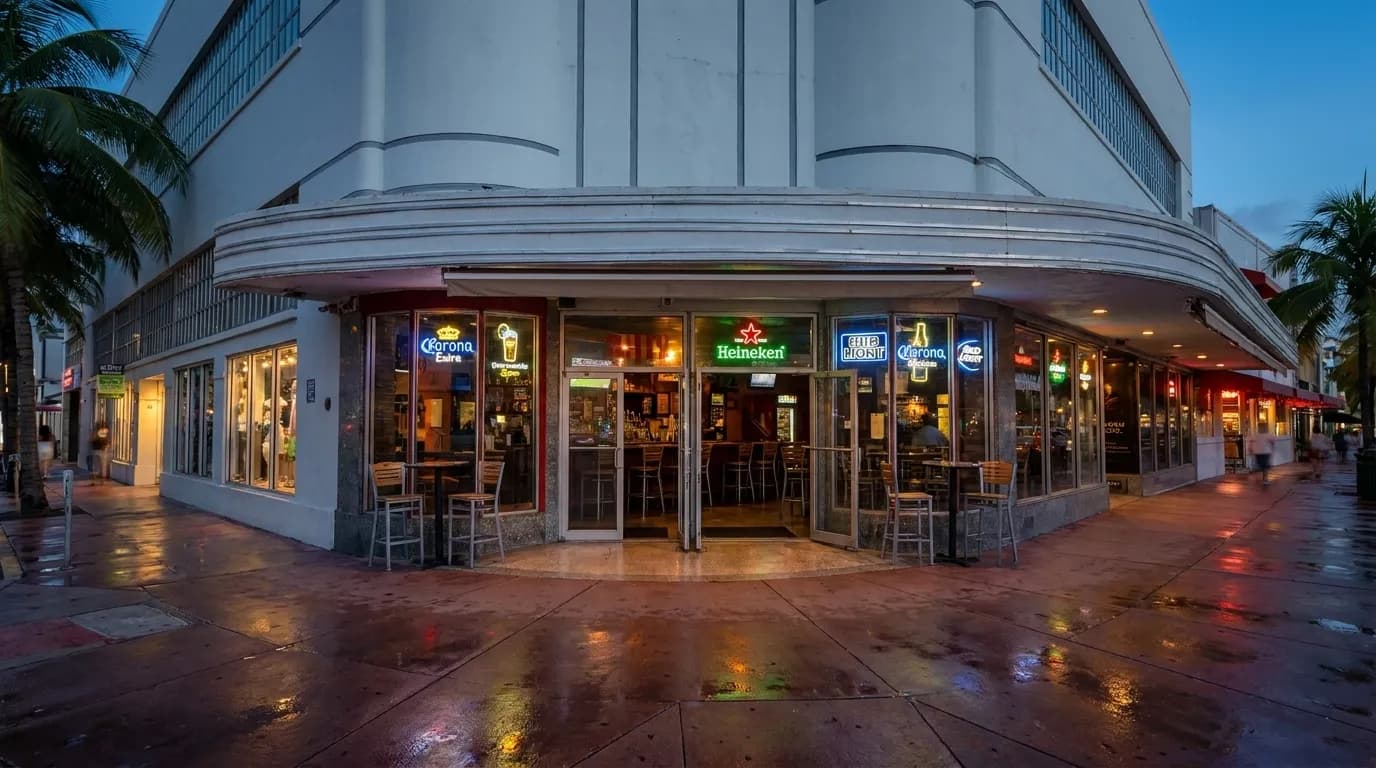 Washington Avenue sidewalk in South Beach at dusk with bar awnings and neon signs glowing