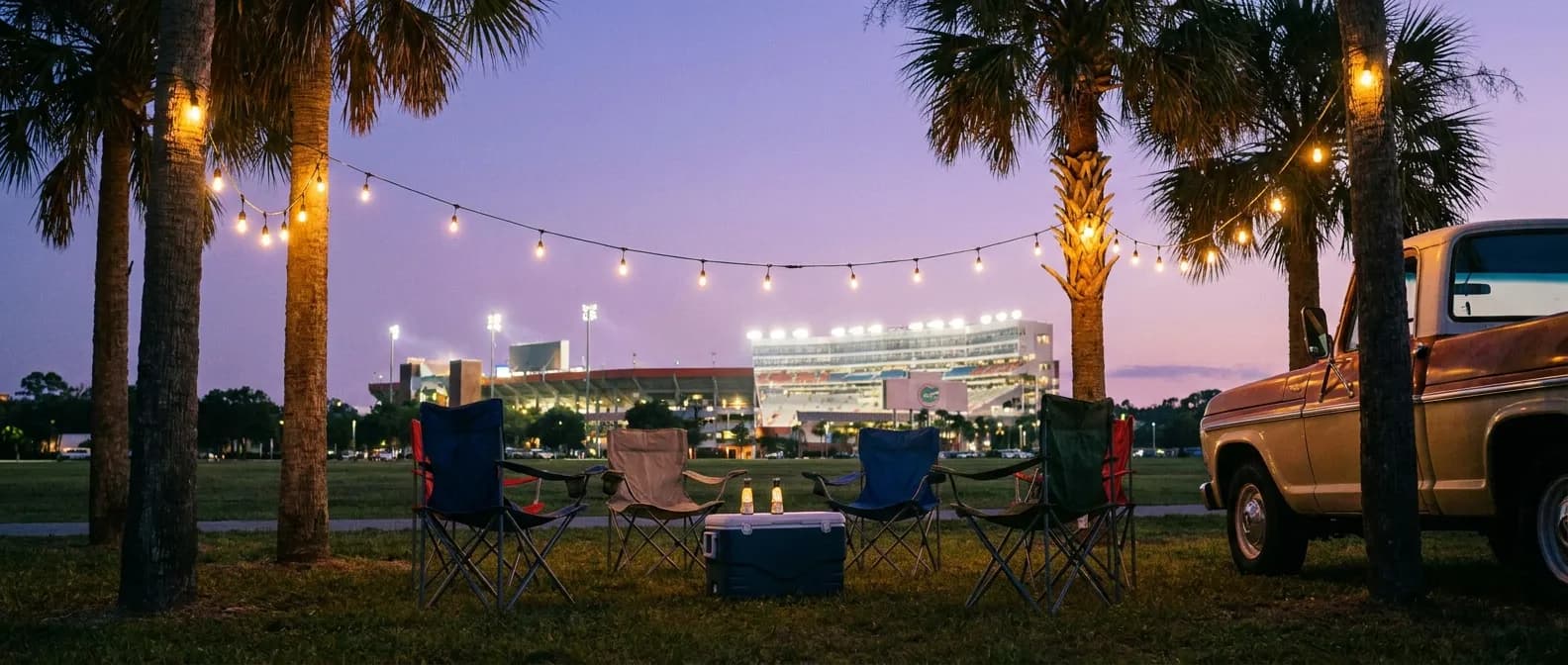 Evening tailgate scene outside a Florida stadium with string lights and folding chairs