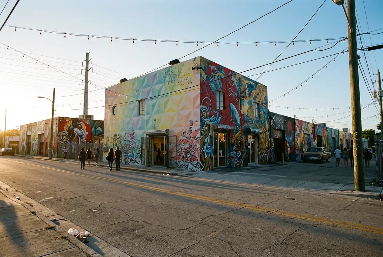 Wide street view of Wynwood's mural-covered warehouse blocks at dusk with pedestrians walking between open gallery doors