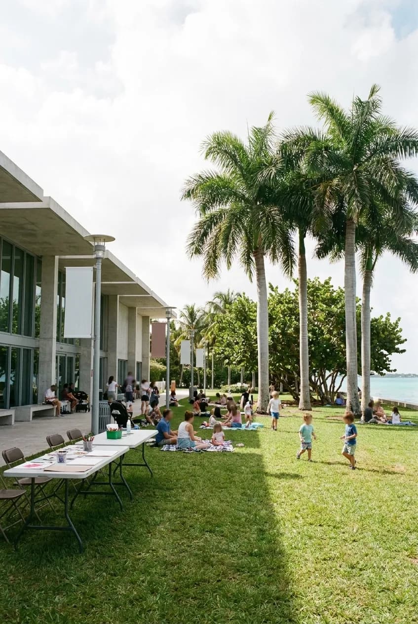 Families spread across the lawn outside a contemporary art museum in Miami on a Saturday morning, art tables set up under palms