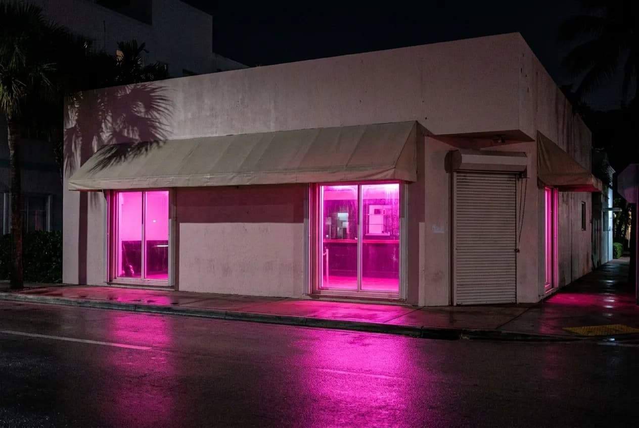 A low corner bar building on a South Beach side street glowing pink from neon window signs after dark