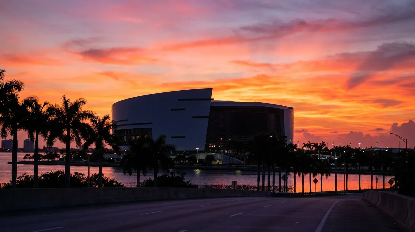 Sun setting behind a Miami stadium exterior with palm trees silhouetted against an orange sky