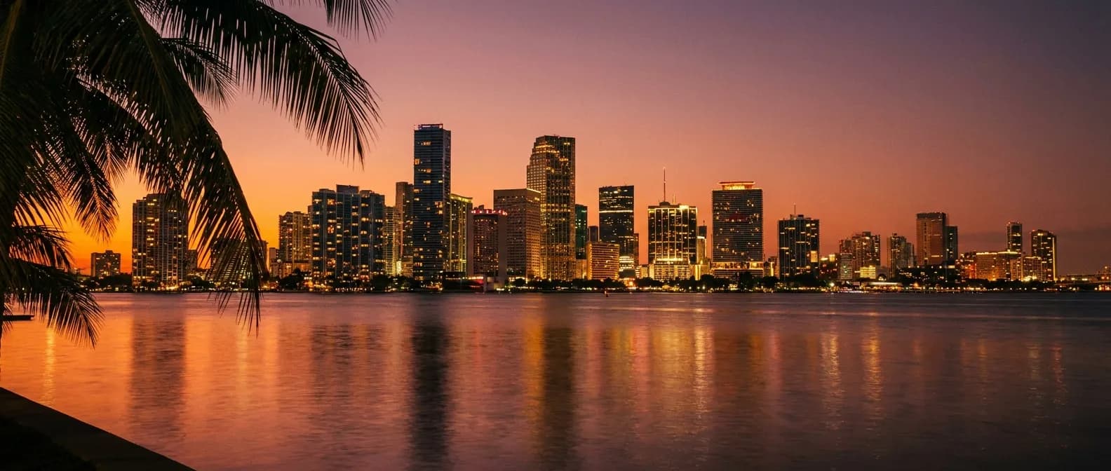 Miami skyline across Biscayne Bay at dusk with warm lights reflecting on the water