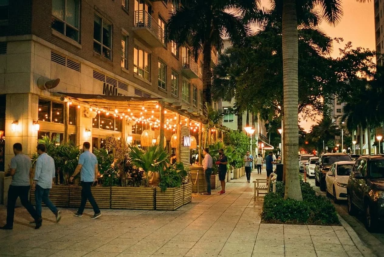 A Midtown Miami street at night with low buildings, string lights and people on the sidewalk