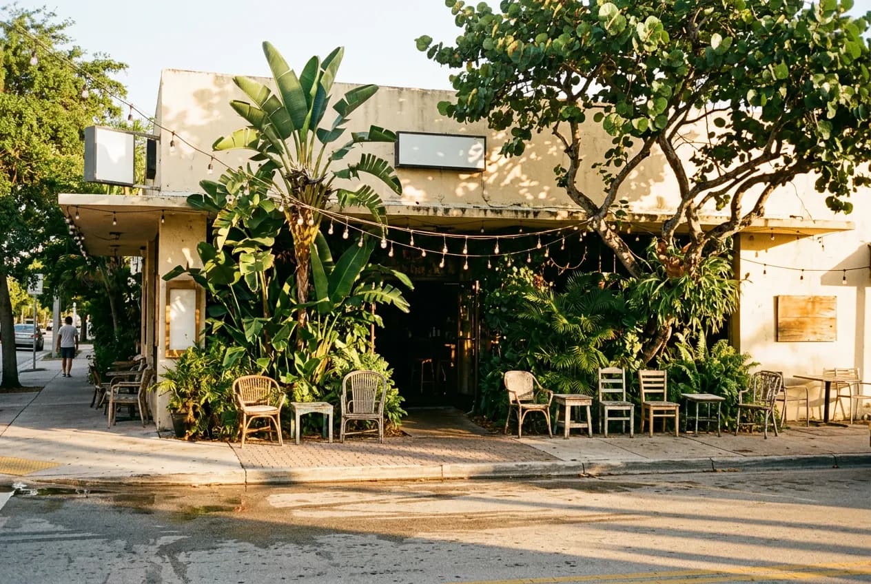 Wide street view of a low-rise Coconut Grove storefront bar with outdoor seating under Miami afternoon light