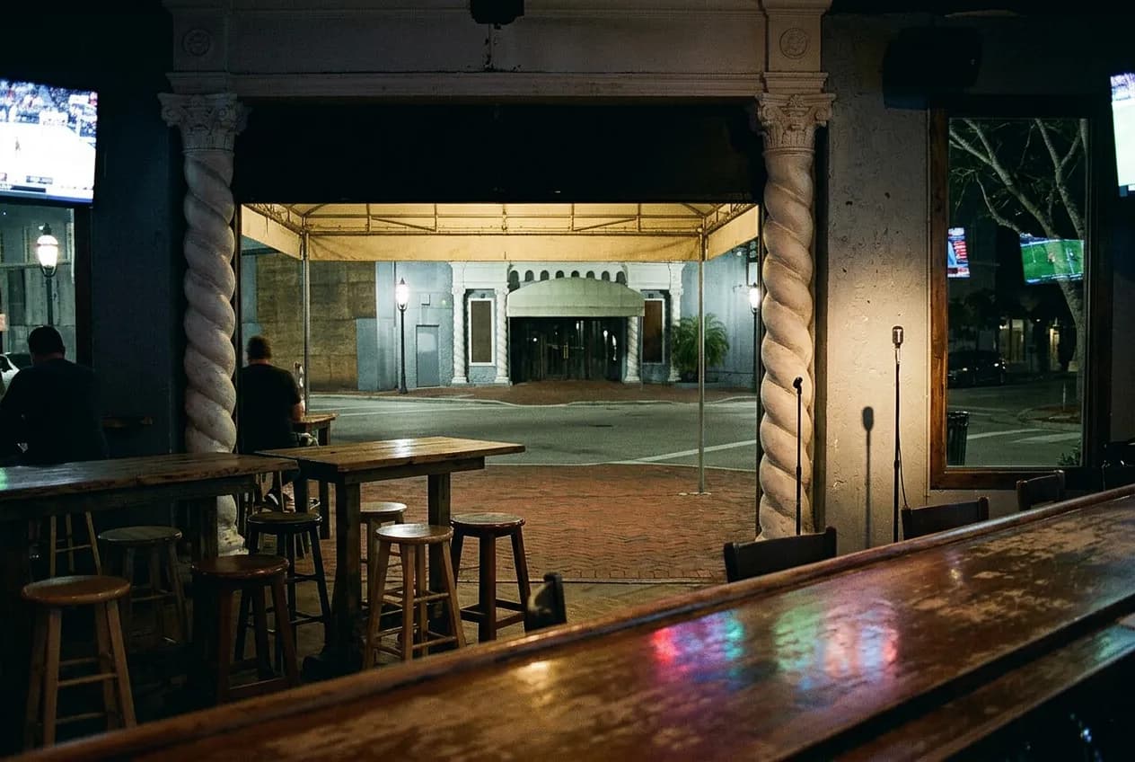 Close interior view of a dim sports-bar seating area with wooden tables and wall-mounted televisions