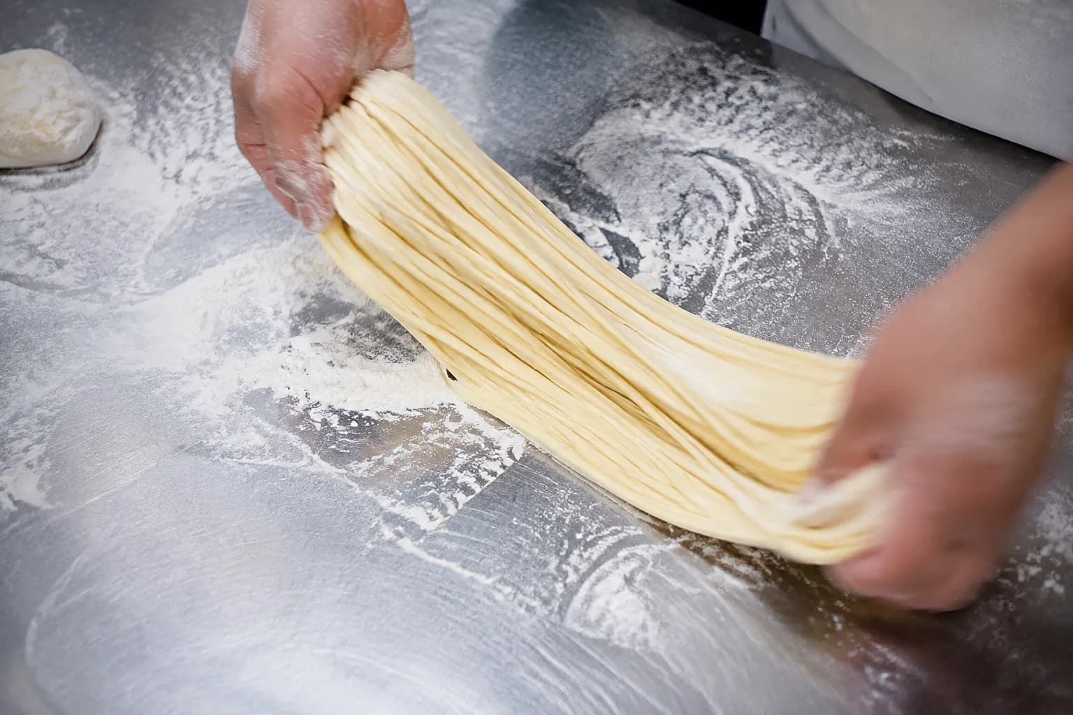 Hands stretching fresh wheat dough for hand-pulled noodles in a Miami Chinese kitchen