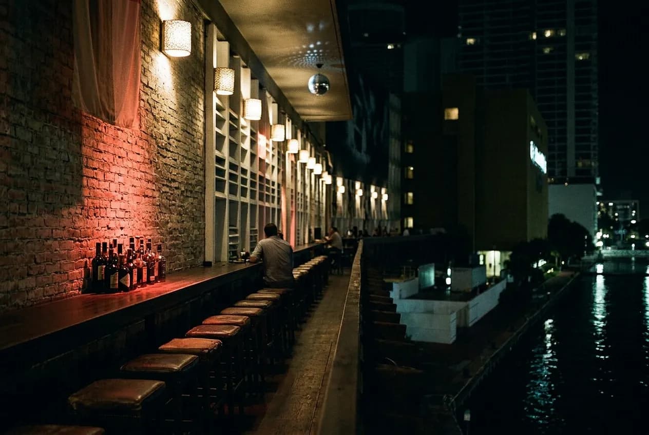 Dim narrow bar interior with leather stools, exposed brick and red-tinted light along a long counter