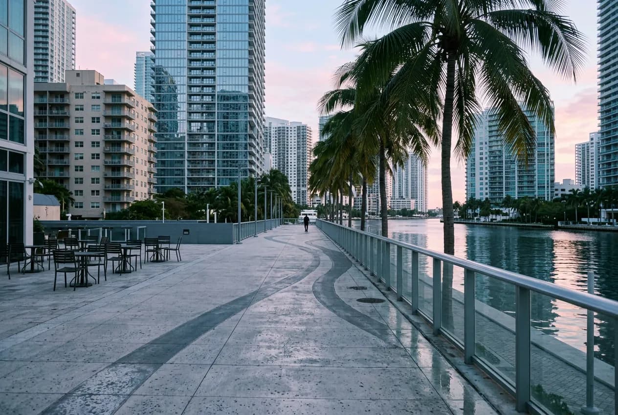 Miami riverfront promenade near Brickell with a waterfront railing and skyline reflections at dawn.