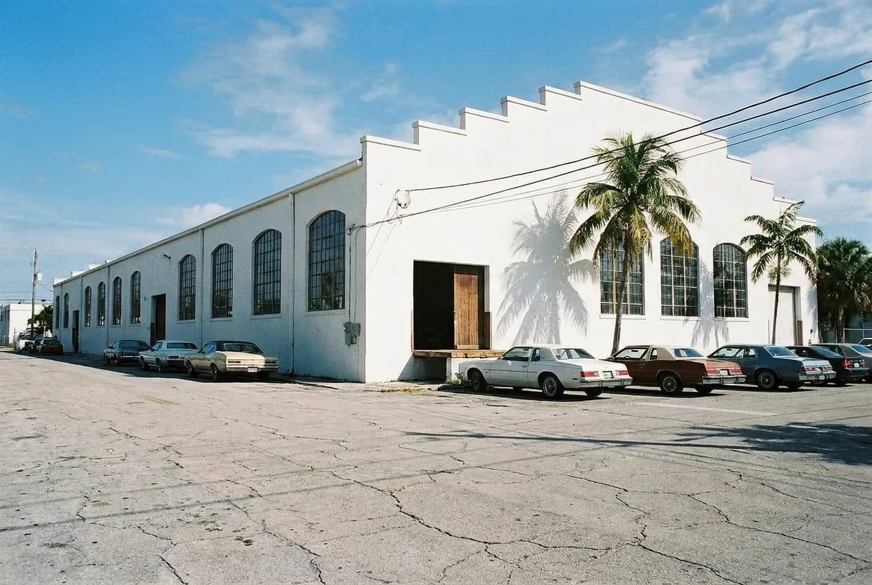 A long low white 1920s industrial building with arched windows under a bright sky