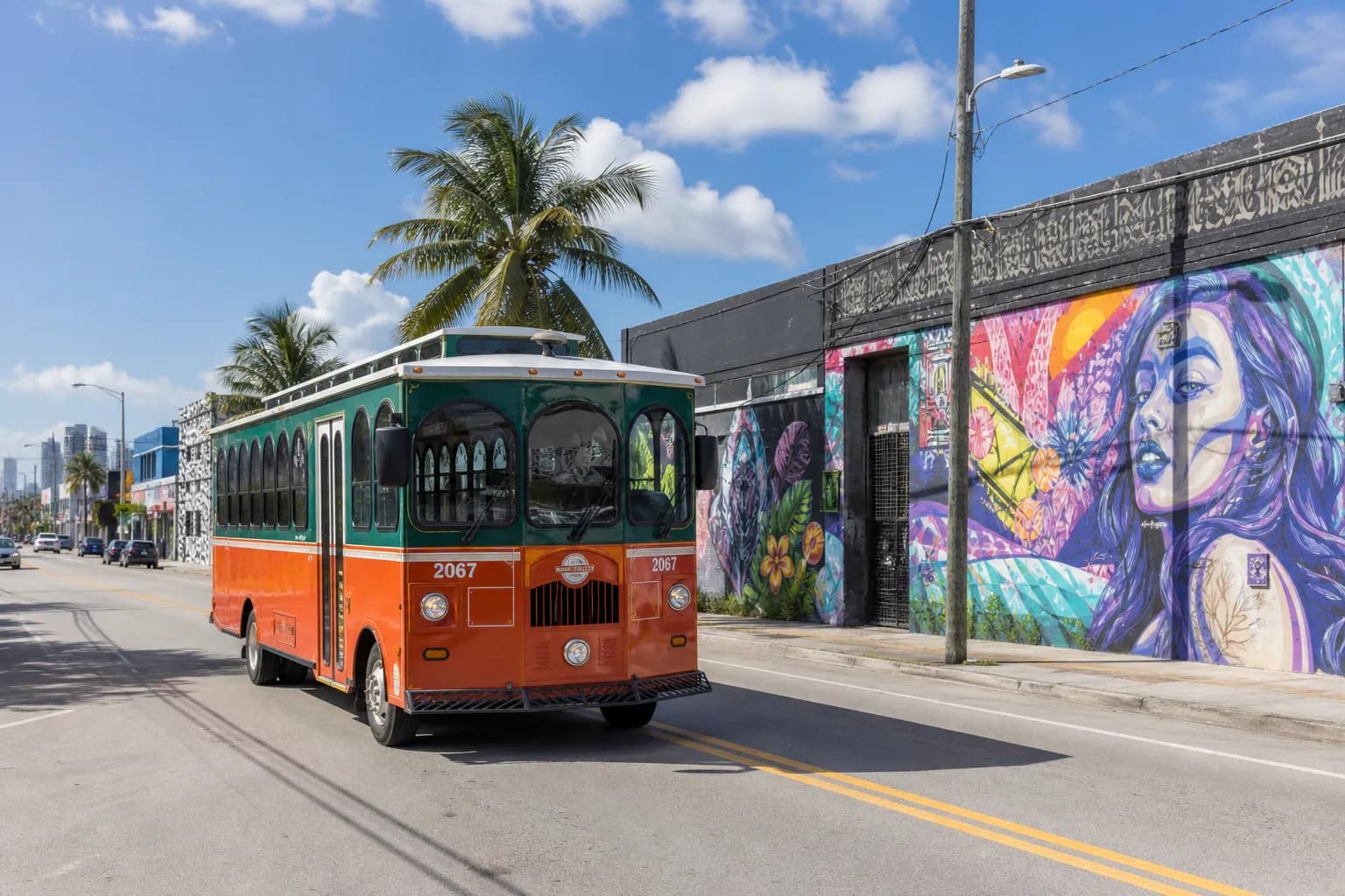 A vintage Miami trolley passing by colorful street murals and pedestrians in the Wynwood Arts District.