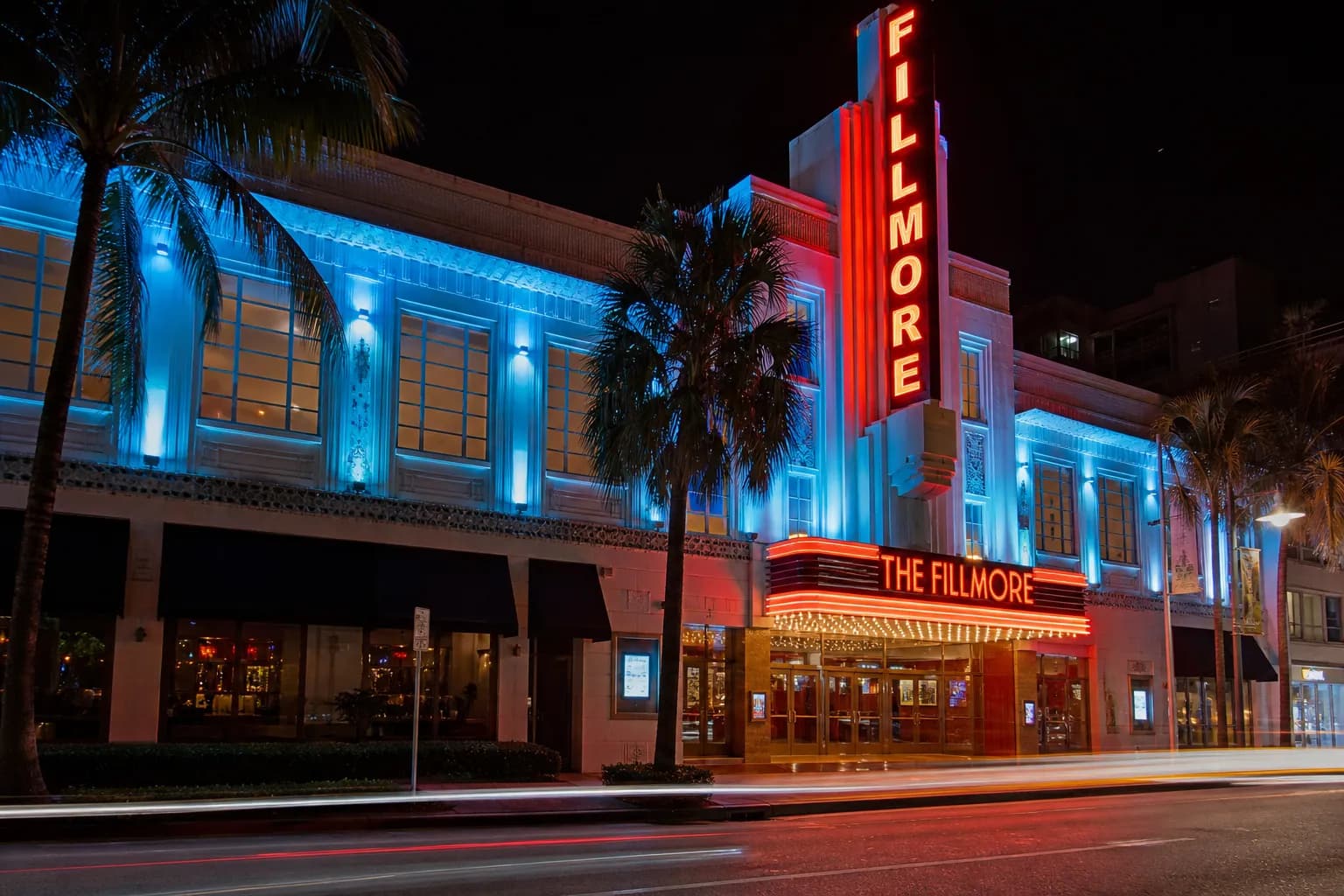 The illuminated Art Deco facade of the Fillmore Miami Beach at night with neon lights and palm trees