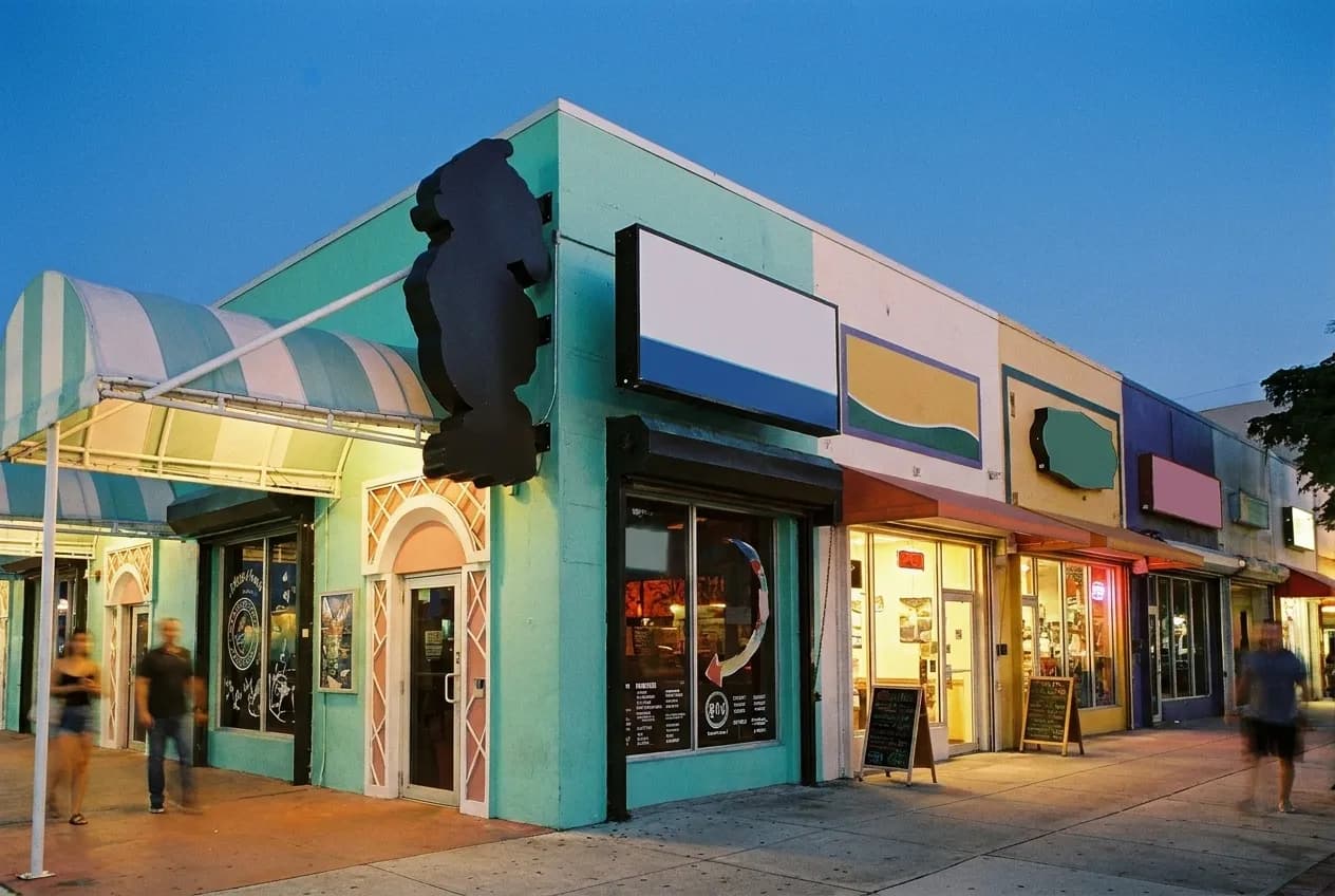 A low commercial street at dusk with lights coming on along the frontages