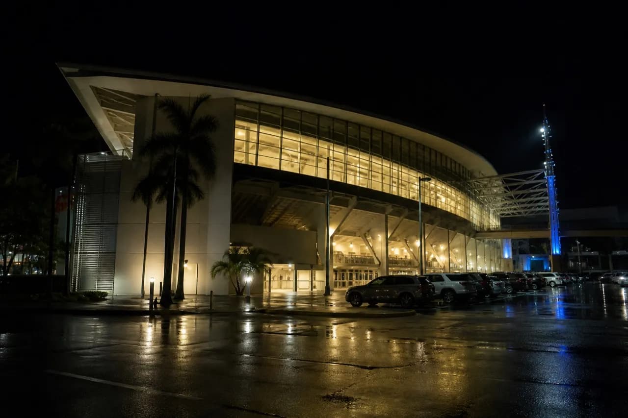 Floodlit stadium structure seen from the parking lot after dark