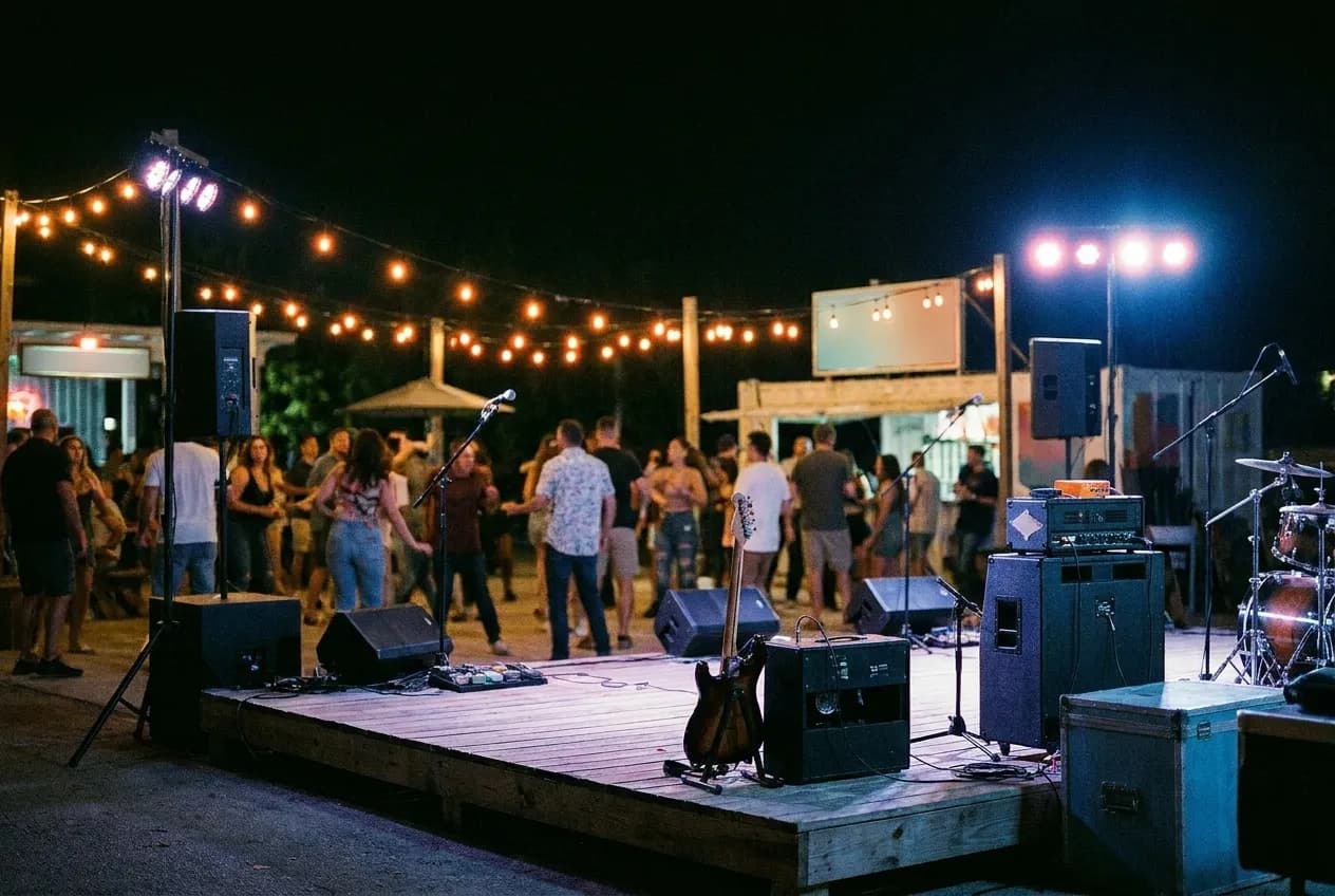 An open-air venue at night, a low stage at one end and lights strung overhead