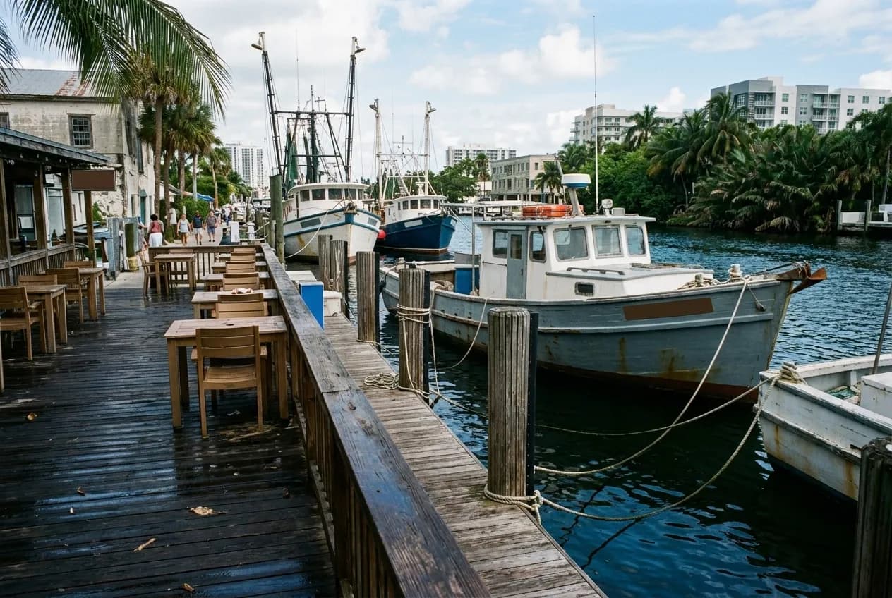 A riverside deck of plain tables with working boats tied up beyond