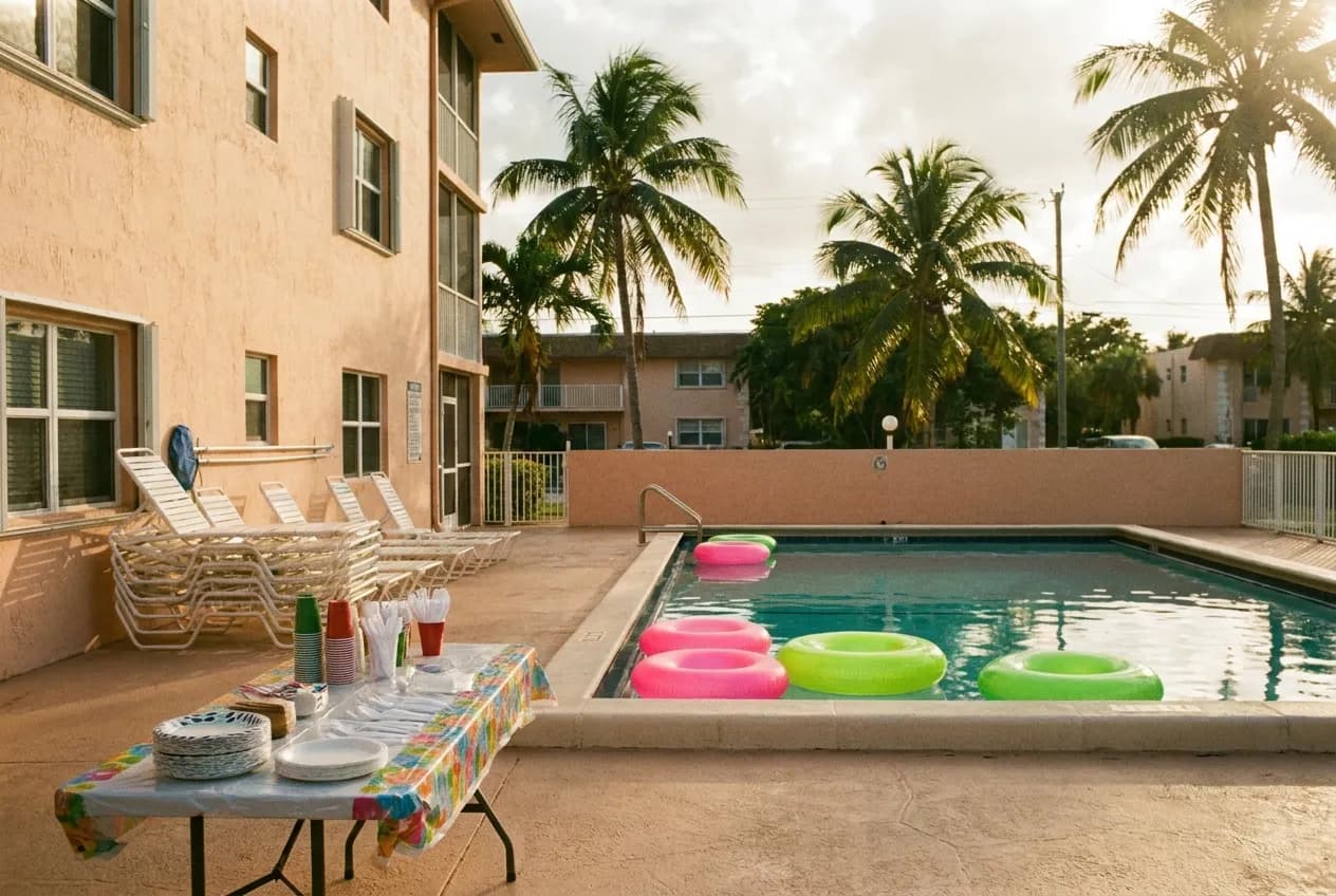 Wide view of a Miami condo pool deck set up for a small party with floats, a folding table of supplies and palm trees in afternoon light