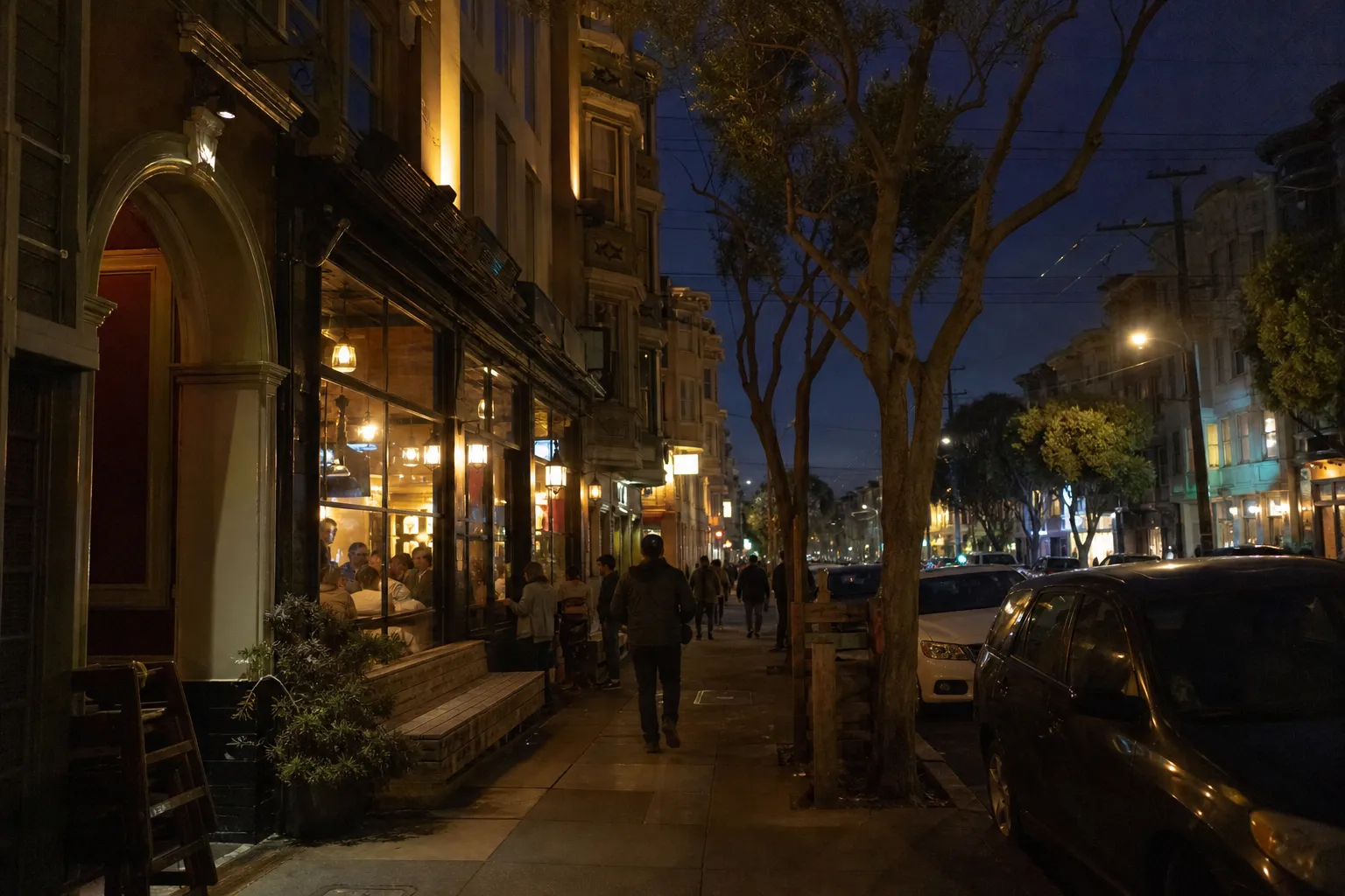 Mission District bar-lined street at night with warm windows and sidewalk traffic