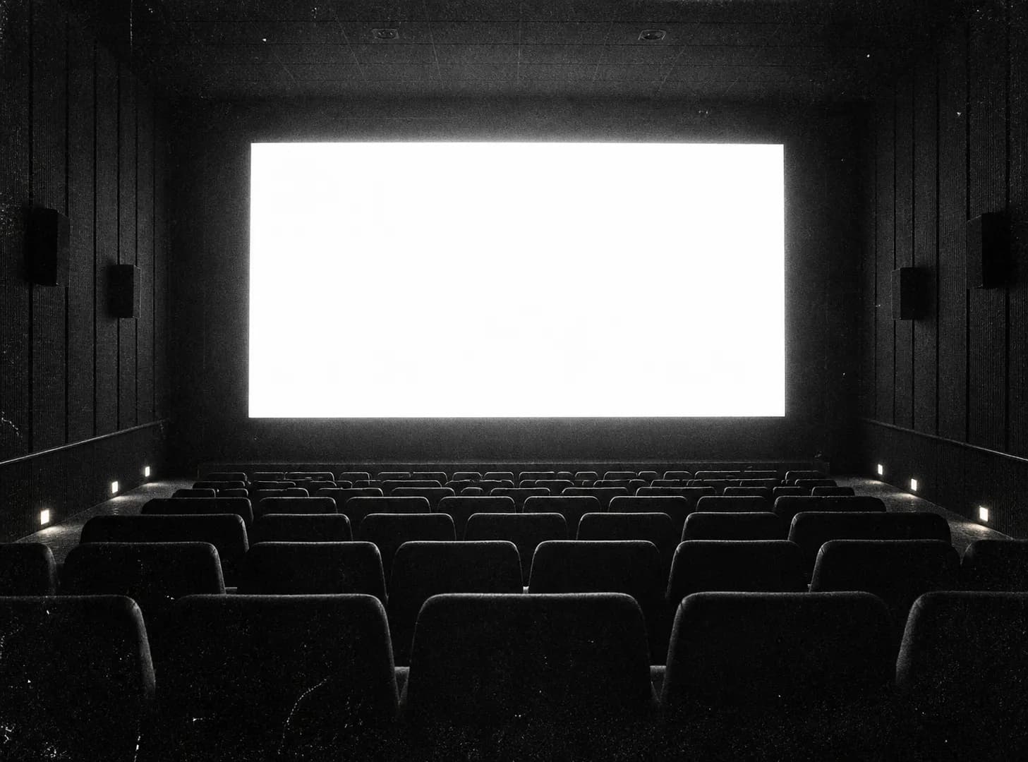 A cinema screen glowing in an empty auditorium with tiered seating in darkness