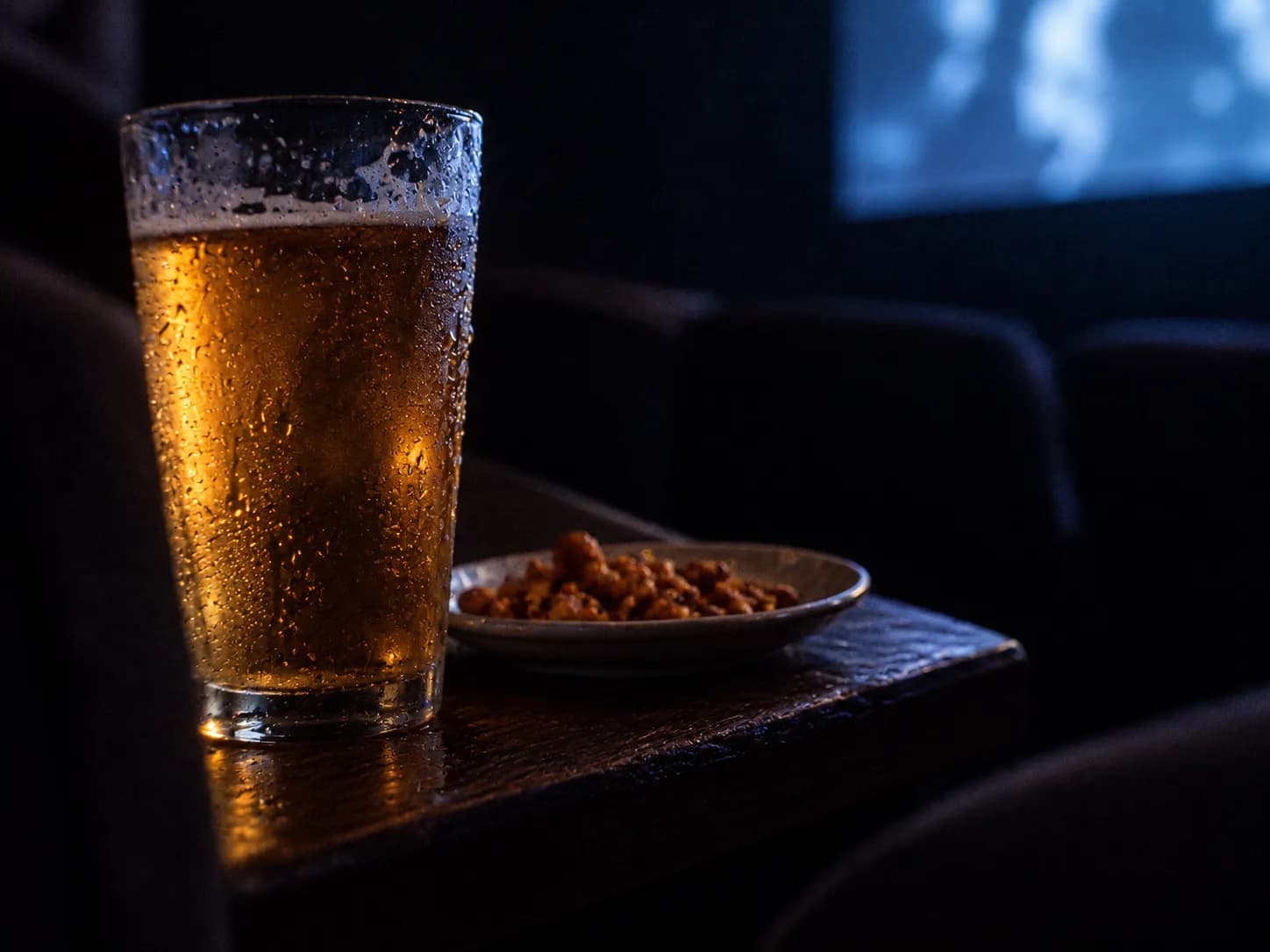A pint glass and a plate on a narrow table in a dark cinema row