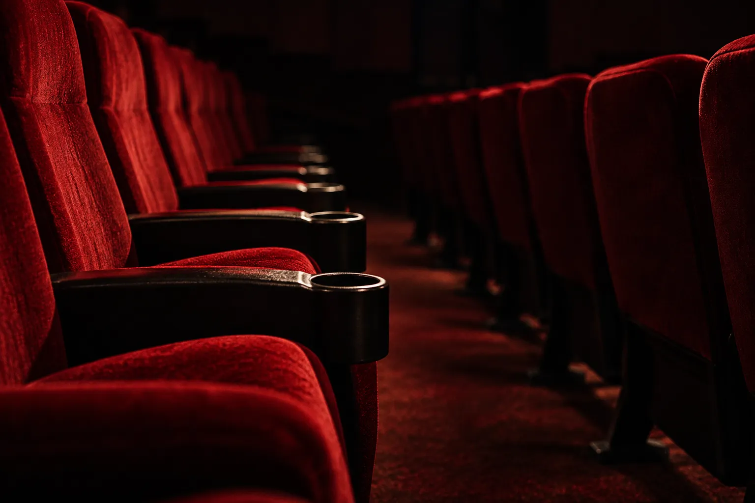 Two rows of empty red cinema seats seen from the side in low light