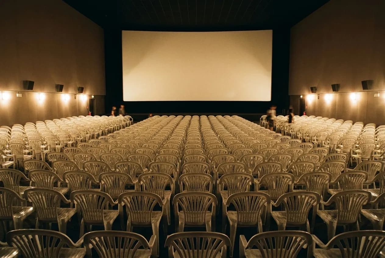 A large empty cinema auditorium seen from the back row, curved screen glowing in low house light