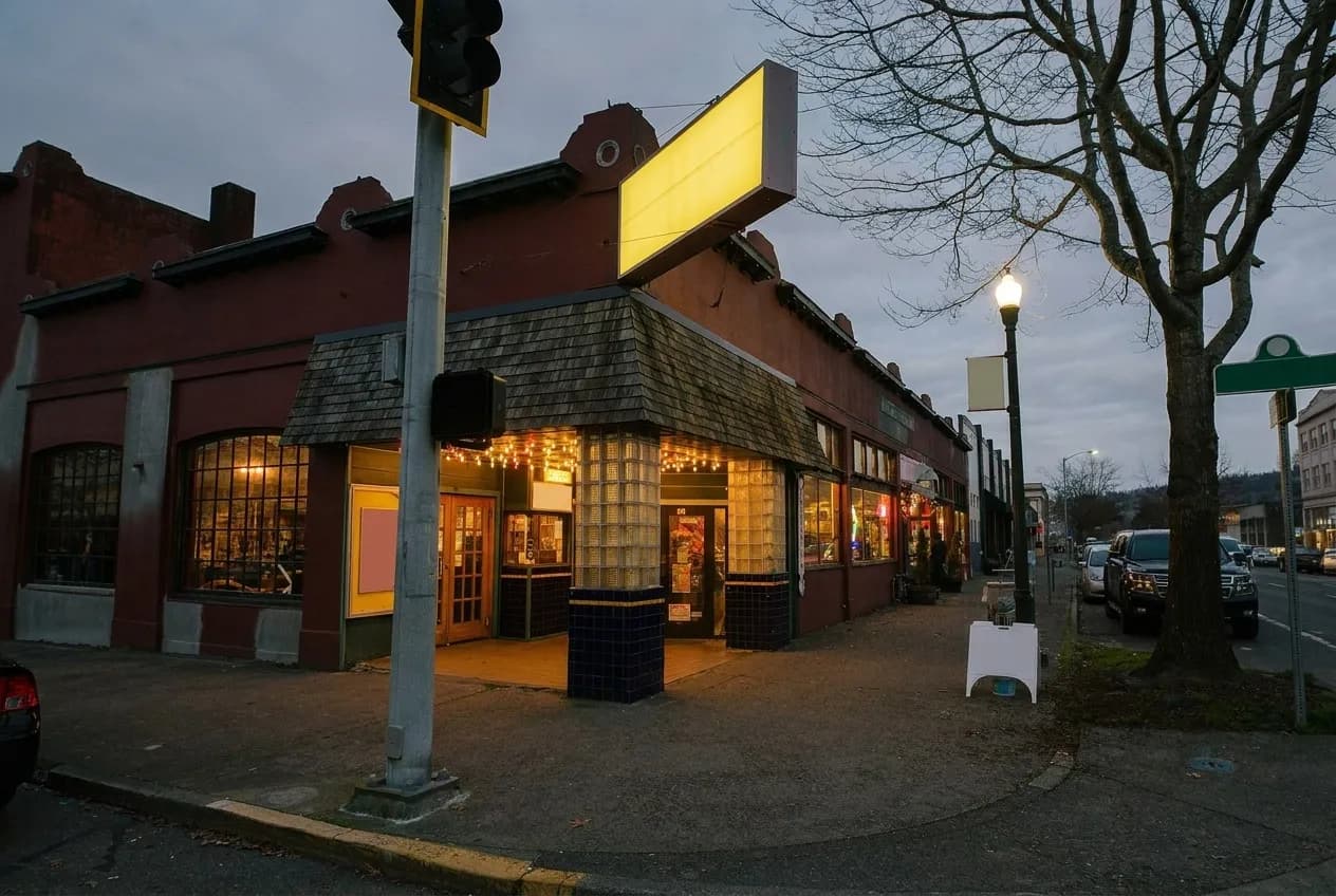 A cinema entrance on a street corner with restaurant windows lit further along