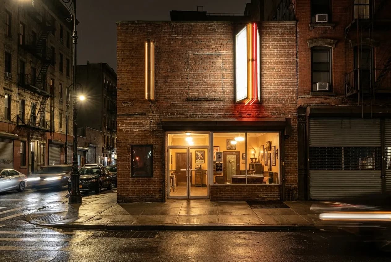 Narrow Lower East Side block after dark with vintage theater entrance lit by warm lobby glow and vertical signage against brick facade