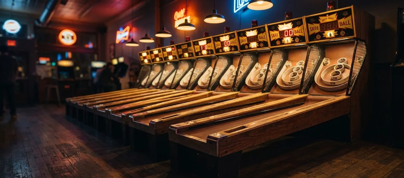Row of illuminated Skee-Ball lanes with scoring displays and wood-paneled alleys in a dimly lit arcade bar