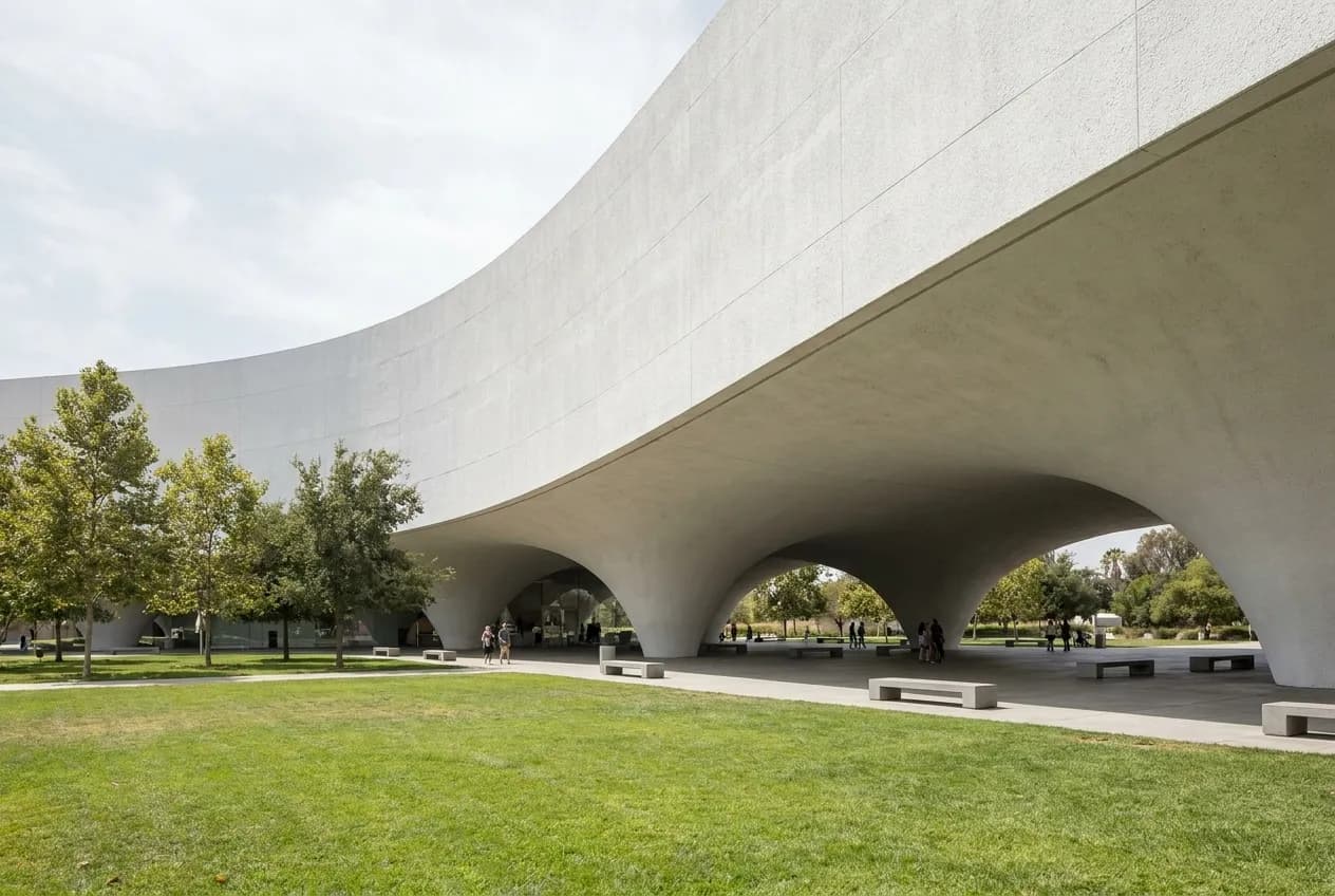 A curving white building with a raised underside over parkland