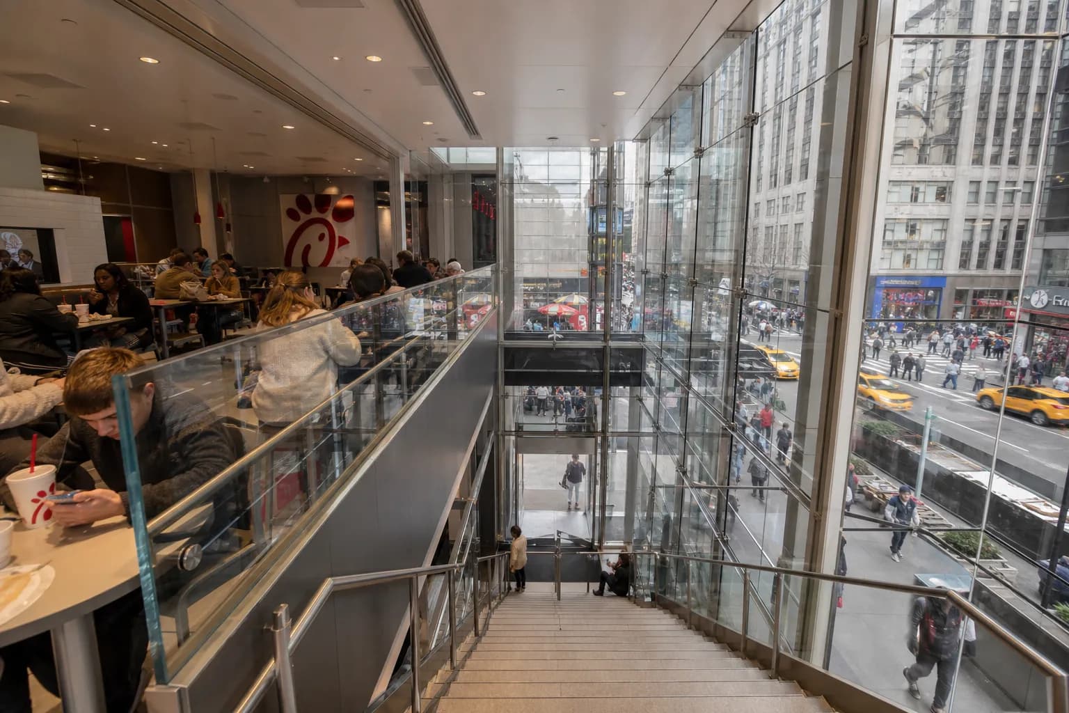 Patrons dining inside a multi-level fast-food restaurant with floor-to-ceiling windows looking out onto a busy Manhattan street.
