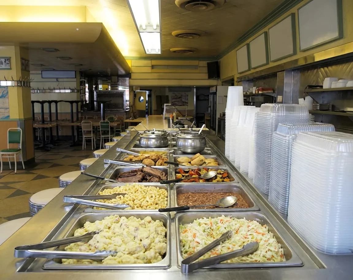 A New York deli salad bar with a long refrigerated buffet of prepared salads and hot dishes and plastic containers stacked at the end