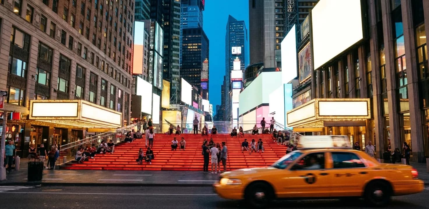 Early evening in the Broadway theater district, red-lit public steps above a plaza with people sitting in small groups, blank glowing marquees along the block and a yellow taxi blurring through the foreground