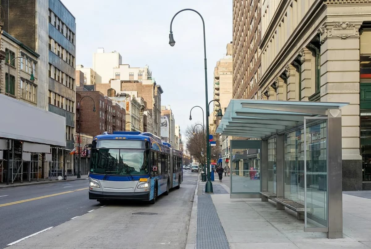 A modern articulated city bus at an upgraded stop with a sheltered waiting area on a wide avenue