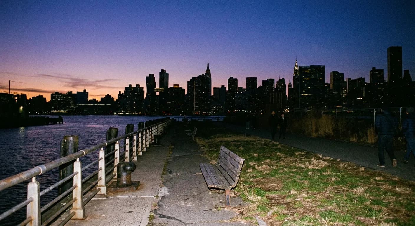 A waterfront promenade at dusk with the city skyline across the water