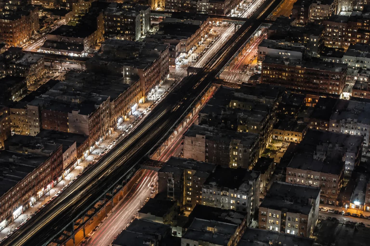Aerial night view of Roosevelt Avenue in Jackson Heights showing elevated subway tracks and surrounding street grid