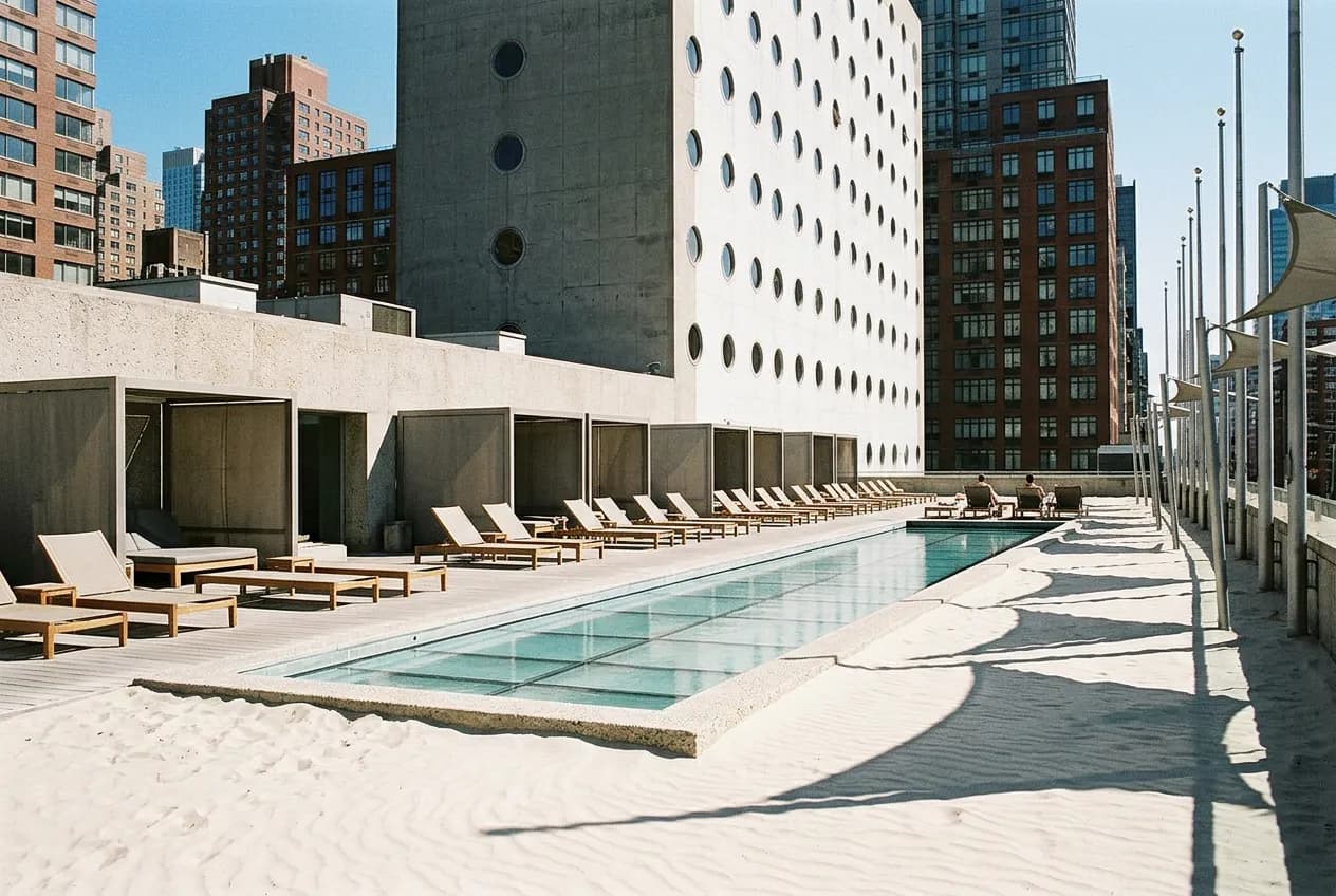 Outdoor hotel pool deck with sand areas and lounge chairs under afternoon light against a Manhattan cityscape.